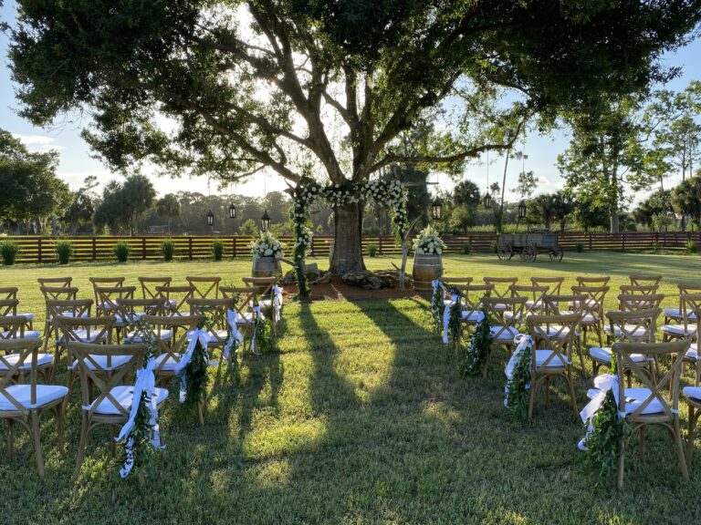 Outdoor wedding ceremony setup under a large tree adorned with floral decorations at a venue near Palm Beach, Florida.