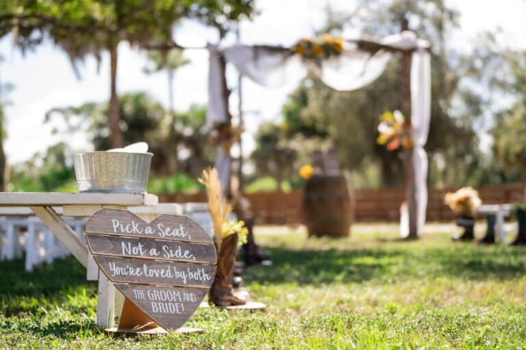 Rustic outdoor wedding ceremony setup near Palm Beach at Rockin H Ranch, featuring a wooden heart sign and decorated arbor under sunny skies.
