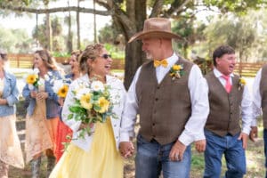 Bride and groom at a ranch wedding near Palm Beach, dressed in Western-inspired attire, surrounded by their wedding party with sunflowers and rustic charm.