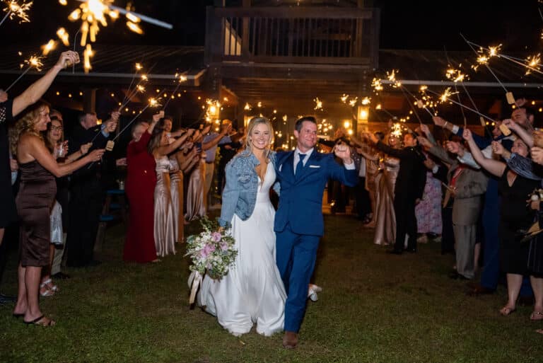 Newlyweds who followed their wedding timeline celebrating a sparkler send-off at their South Florida ranch, with the bride in a denim jacket and the groom in a navy suit.