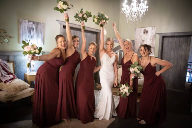 The bride and bridesmaids in burgundy dresses celebrating indoors with floral bouquets at a South Florida ranch wedding.