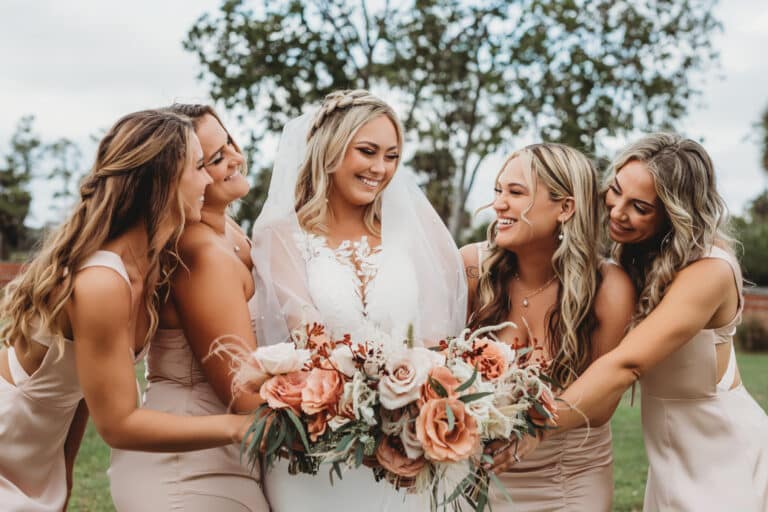 A bride surrounded by her bridesmaids holding a floral bouquet crafted by a local florist, set against the backdrop of a picturesque South Florida ranch wedding.