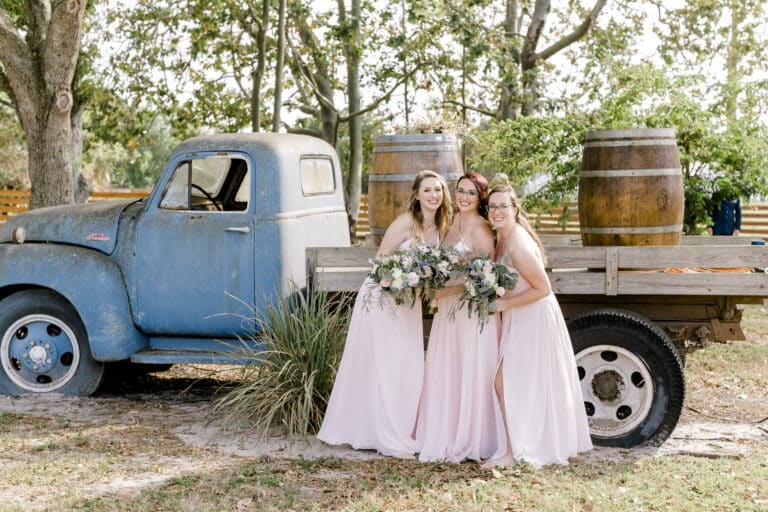 Bridesmaids in blush dresses pose by a vintage blue truck at Rockin H Ranch, a top venue for outdoor wedding ceremonies near Palm Beach.