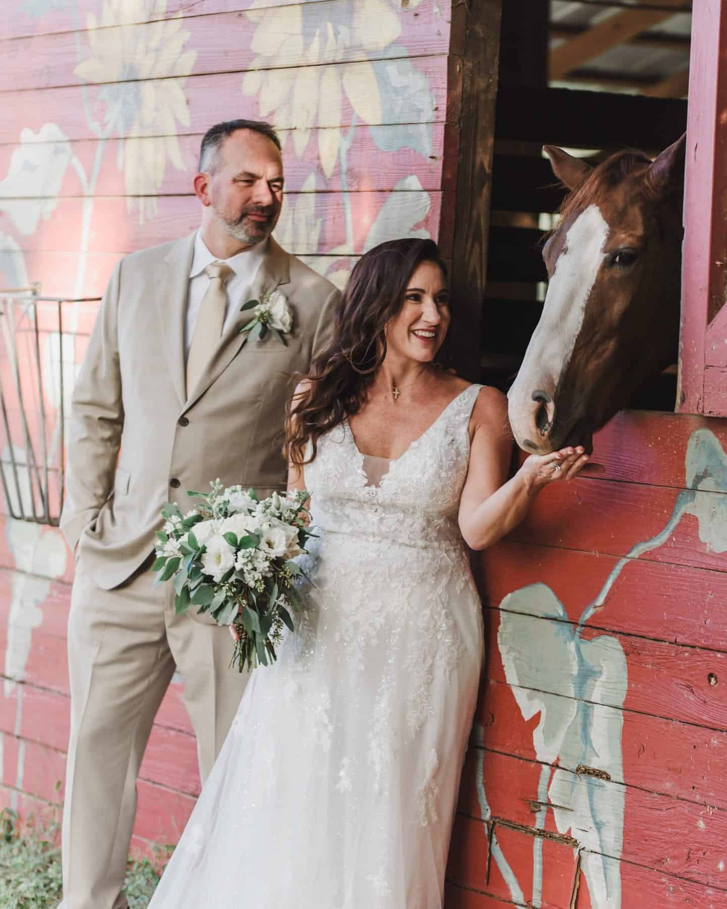 Wedding couple feeding horse in barn on beautiful ranch venue